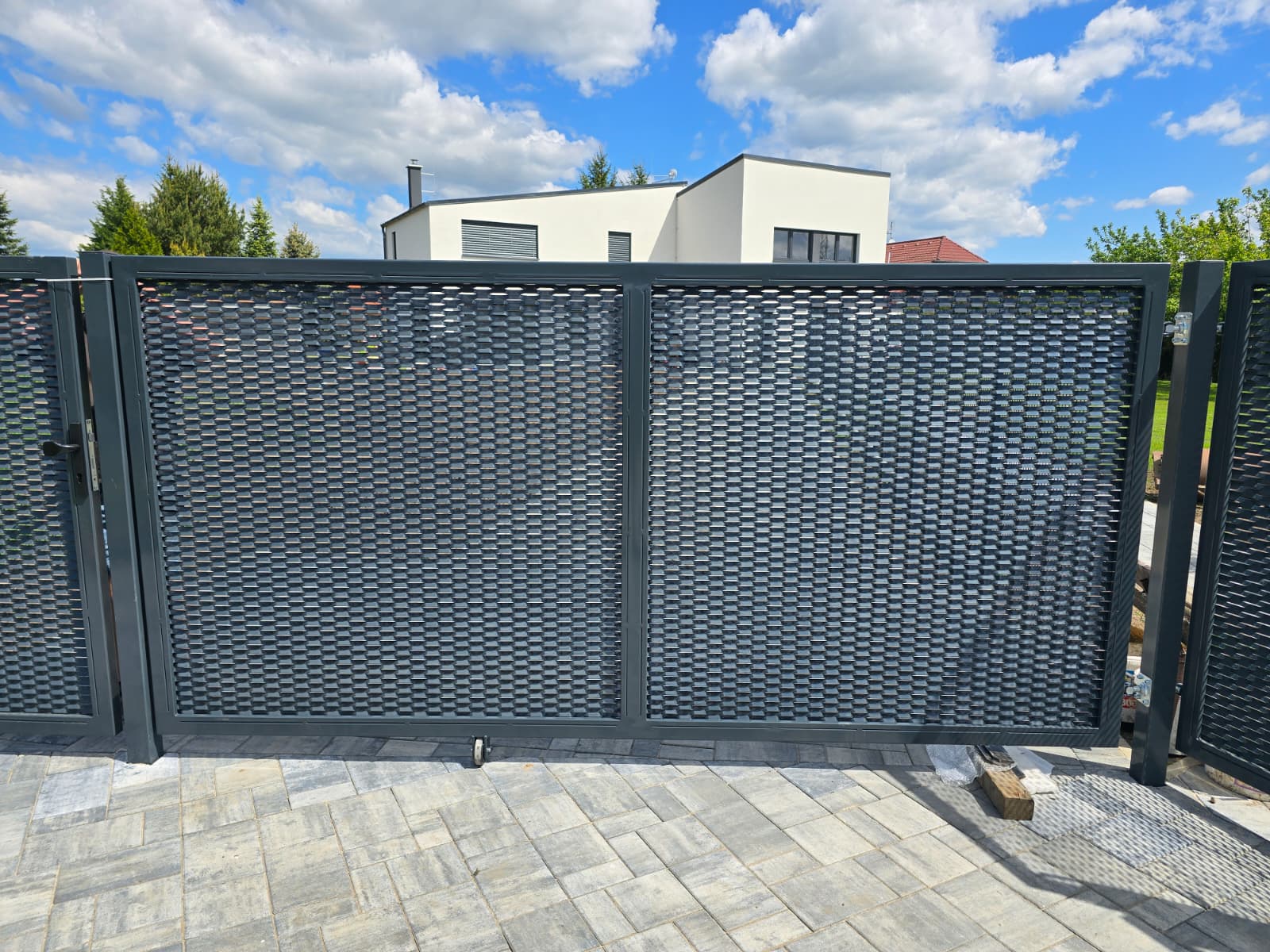 Antracitová posuvná brána s děrovanou výplní před bílým domem
